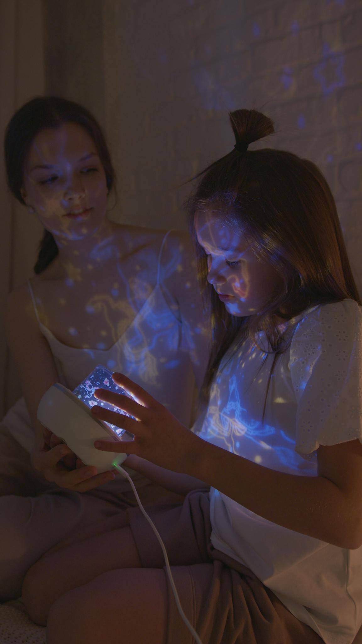 A mother and daughter bonding while enjoying a starry night light in their cozy bedroom.